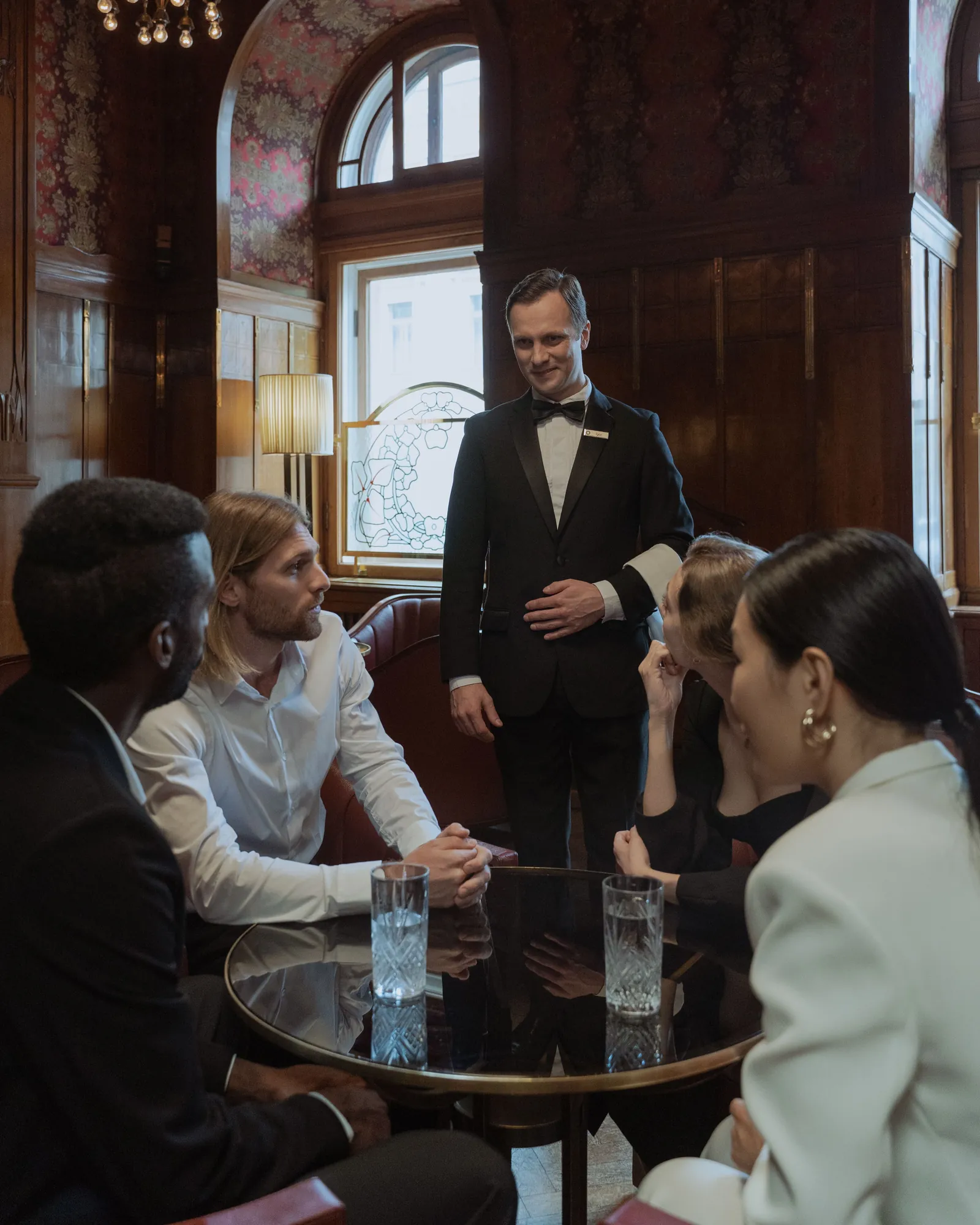 Host in a dinner jacket addressing guests in a panelled room